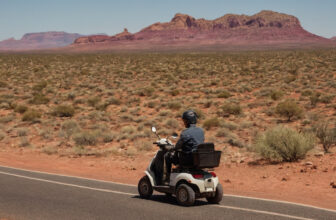 Rider on a mobility scooter on a desert road with red rock mesas in the distance