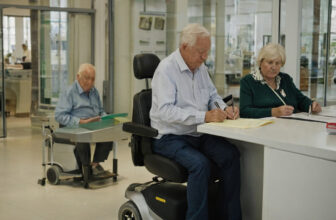 Older customers signing paperwork at a dealer's desk with a mobility scooter beside them