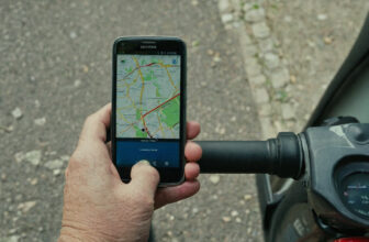 Hand holding a smartphone showing a map beside the tiller of a mobility scooter