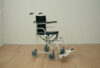 Transport chair with four small wheels and long push handles, seen from the side