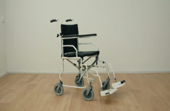 Transport chair with four small wheels and long push handles, seen from the side
