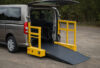 Vehicle wheelchair lift with yellow side barriers at the rear of a van, platform lowered with its outer ramp down to the ground