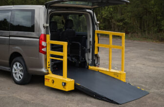 Vehicle wheelchair lift with yellow side barriers at the rear of a van, platform lowered with its outer ramp down to the ground